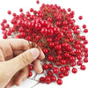 Una mano sostiene un racimo de bayas de acebo artificiales de color rojo brillante para decoración navideña.