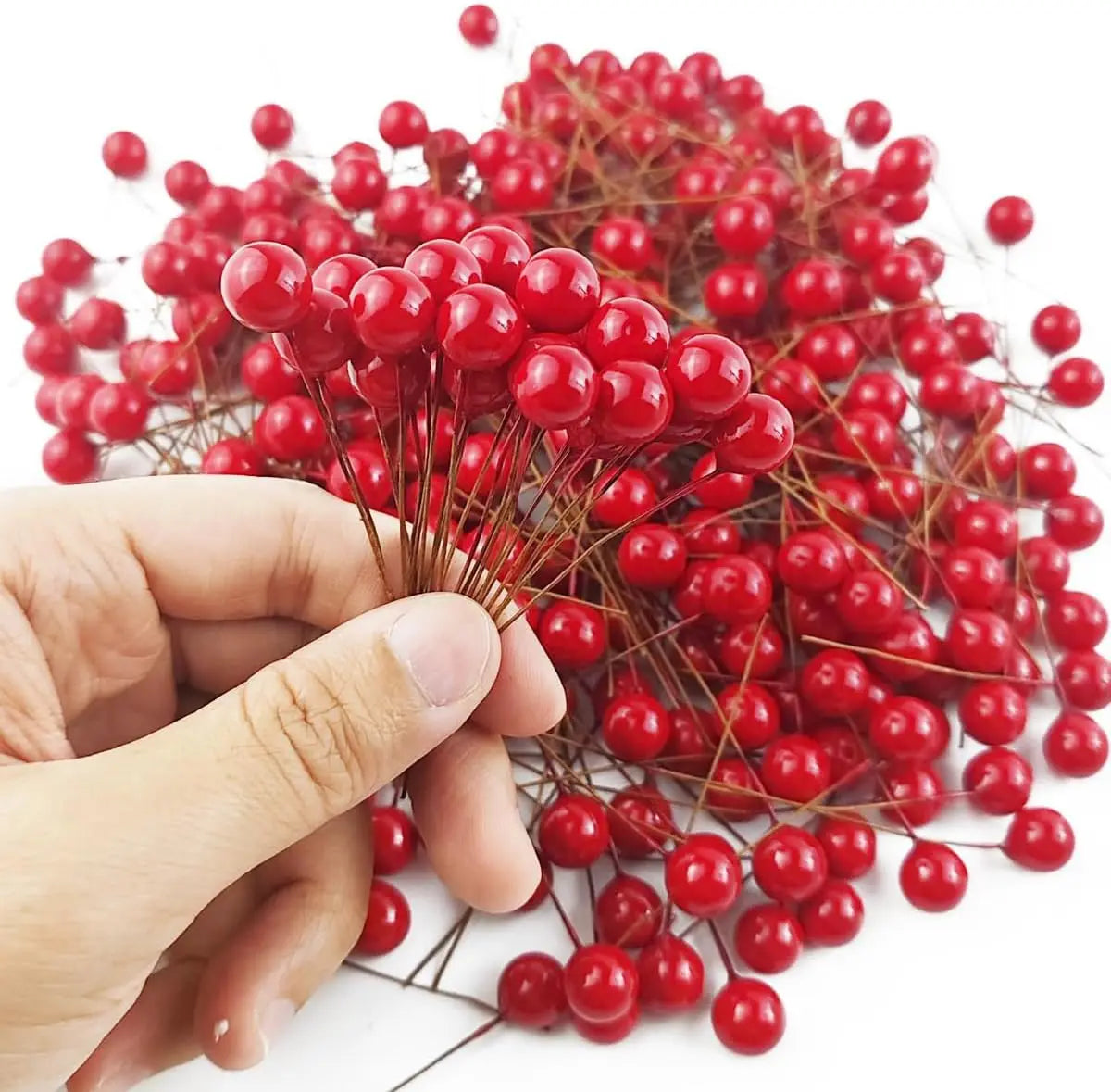 Una mano sostiene un racimo de bayas de acebo artificiales de color rojo brillante para decoración navideña.