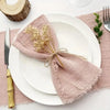 A stack of ten handcrafted fringed cotton napkins in a dusty rose color placed on white plates.