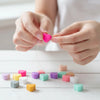 Hands are making a pink silicone heart bead for DIY jewelry making on a white wooden surface.