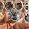 A hand holds a commemorative coin featuring the image of Saint Michael the Archangel.