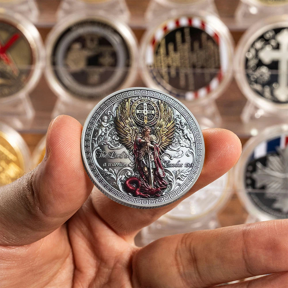 A hand holds a commemorative coin featuring the image of Saint Michael the Archangel.