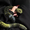 A hand holds a green snake art model against a black fabric background.