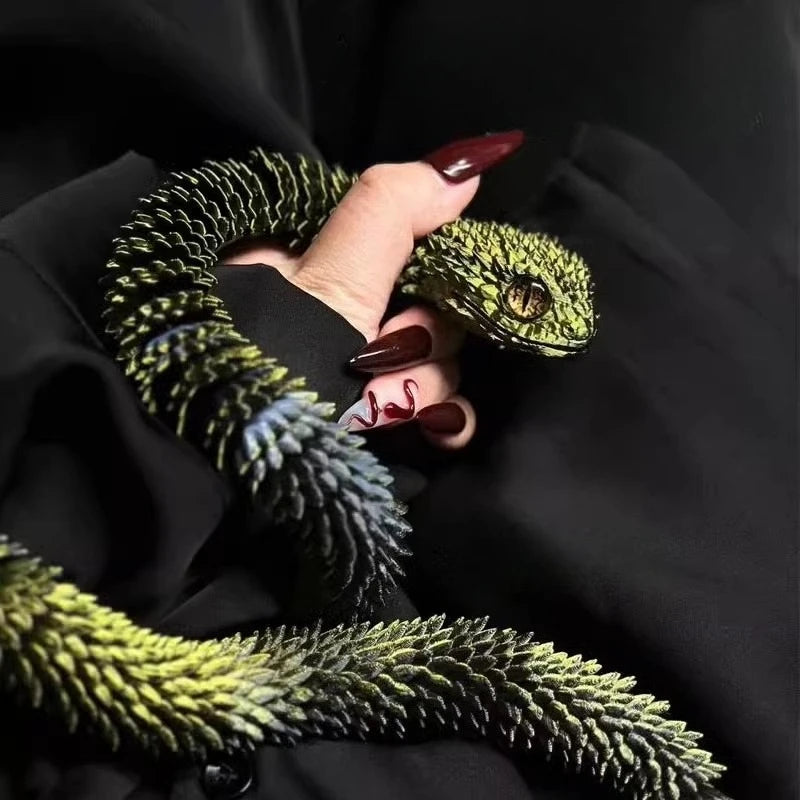 A hand holds a green snake art model against a black fabric background.