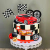 A tiered cake topper featuring a red racing car, checkered flags, and various wheels on a black and white striped background.