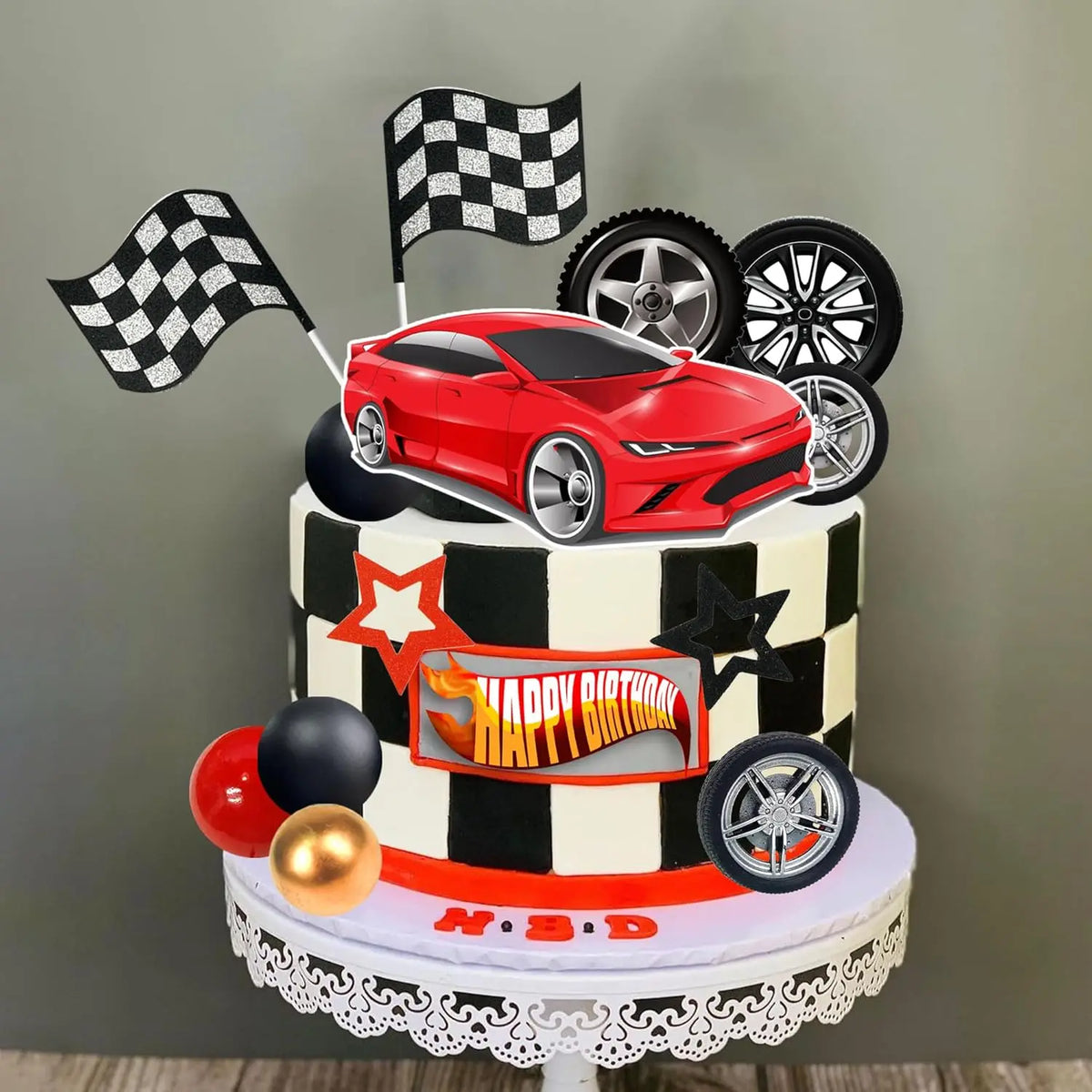A tiered cake topper featuring a red racing car, checkered flags, and various wheels on a black and white striped background.
