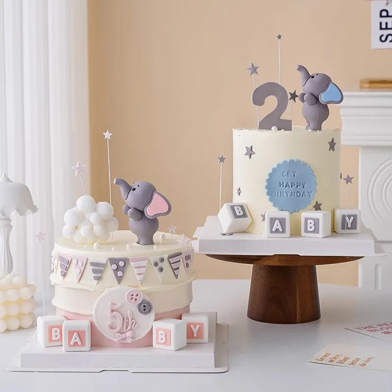 A tiered birthday cake decorated with gray elephant toppers and pastel accents on a white table.