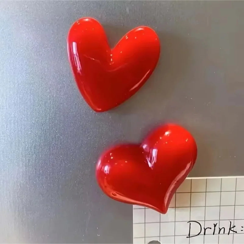 Two glossy red heart-shaped fridge magnets against a gray background.