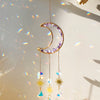 A handcrafted moon crystal suncatcher featuring a gold pendant and purple crystals hanging against a bright background.