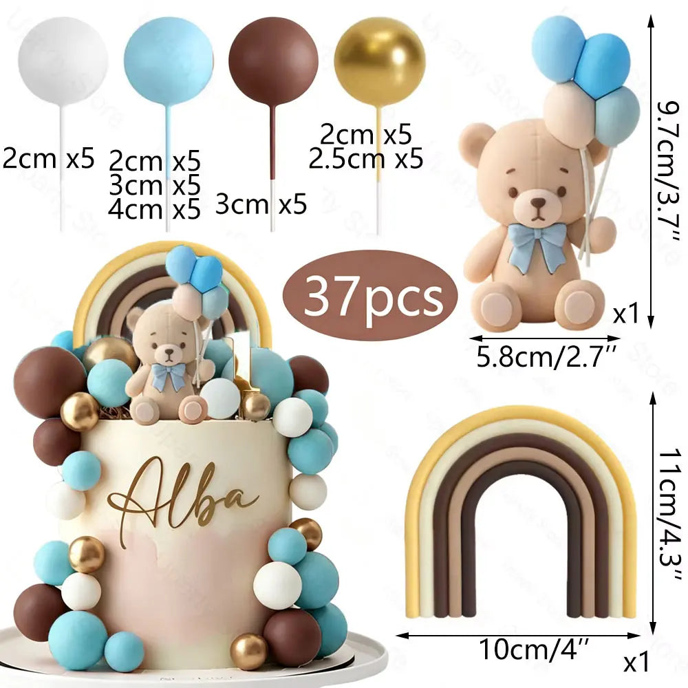 A teddy bear cake topper featuring blue and white foam balls and a rainbow arch.