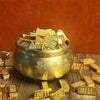 A golden bowl filled with small gold bar pattern decor pieces resting on a dark wooden surface.