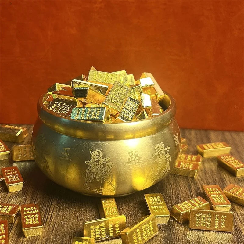 A golden bowl filled with small gold bar pattern decor pieces resting on a dark wooden surface.