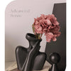 A black ceramic figural vase holding pink hydrangeas on a light surface.
