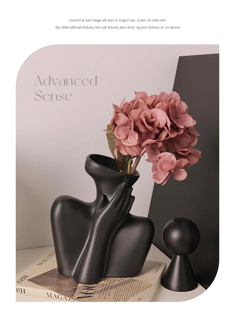 A black ceramic figural vase holding pink hydrangeas on a light surface.