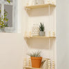 A rustic wooden wall shelf with multiple hanging shelves displaying decorative items like a ceramic face, potted plants, and 