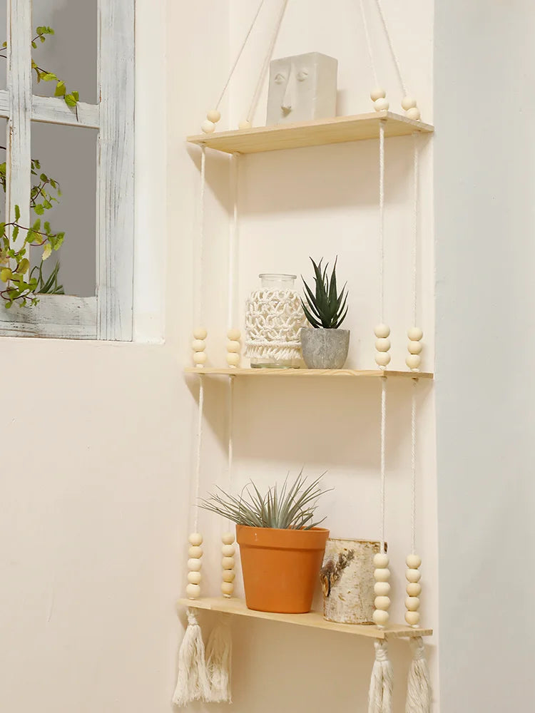 A rustic wooden wall shelf with multiple hanging shelves displaying decorative items like a ceramic face, potted plants, and 