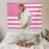 Un homme en chemise claire pose devant une décoration murale de drapeau américain rayé rose et blanc.