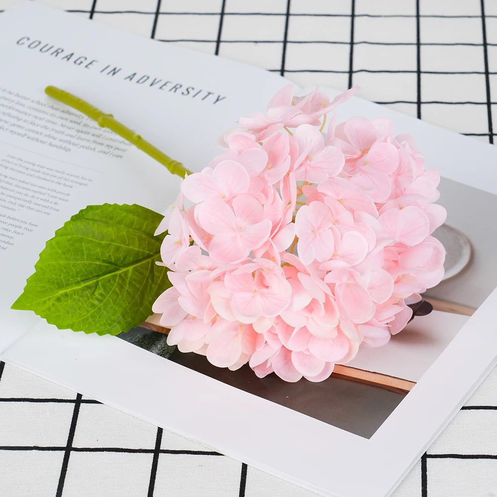 A close-up photo of a large cluster of pink artificial hydrangea flowers resting on a white page with text.