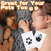 A baby is gently touching a black ink paw print on a white card next to a dog's paw.