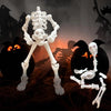 A white plastic skeleton figurine standing upright in front of a carved pumpkin and shadowy figures.
