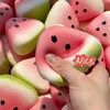 A hand is squeezing a pink and green cat paw shaped squishy toy with black dots.