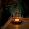 A vintage wooden candle lantern with a glass cover burning a white candle on a wooden surface.