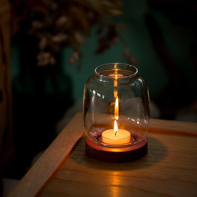 A vintage wooden candle lantern with a glass cover burning a white candle on a wooden surface.
