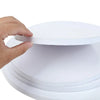 A hand is lifting a round white corrugated cake board from a stack of similar boards.