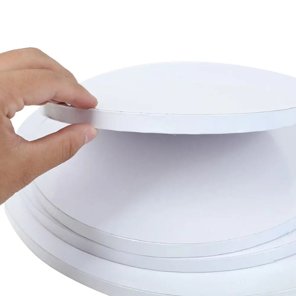 A hand is lifting a round white corrugated cake board from a stack of similar boards.
