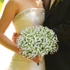 A woman holds a bouquet of white baby's breath flowers against a dark suit jacket.