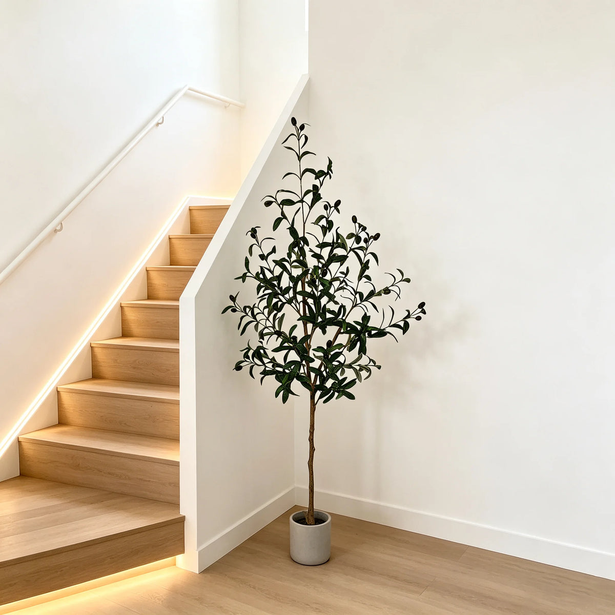 A tall artificial olive tree in a pot stands next to a modern staircase with illuminated steps.