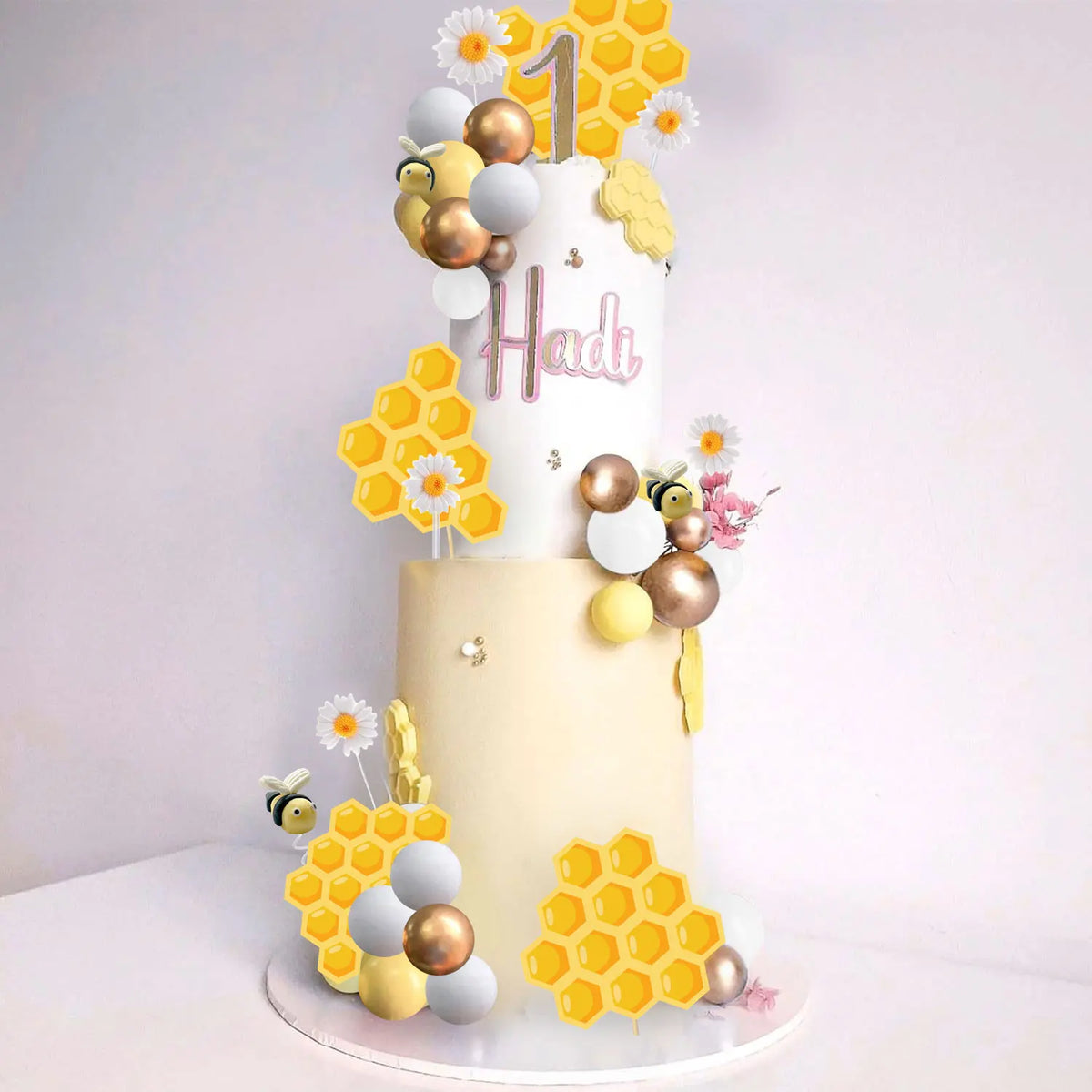 A tiered cake decorated with gold and white honeycomb shapes, spheres, and flowers, featuring the number one and the name Had