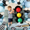 A race car shaped balloon is positioned in front of a black traffic light balloon set and a young child.