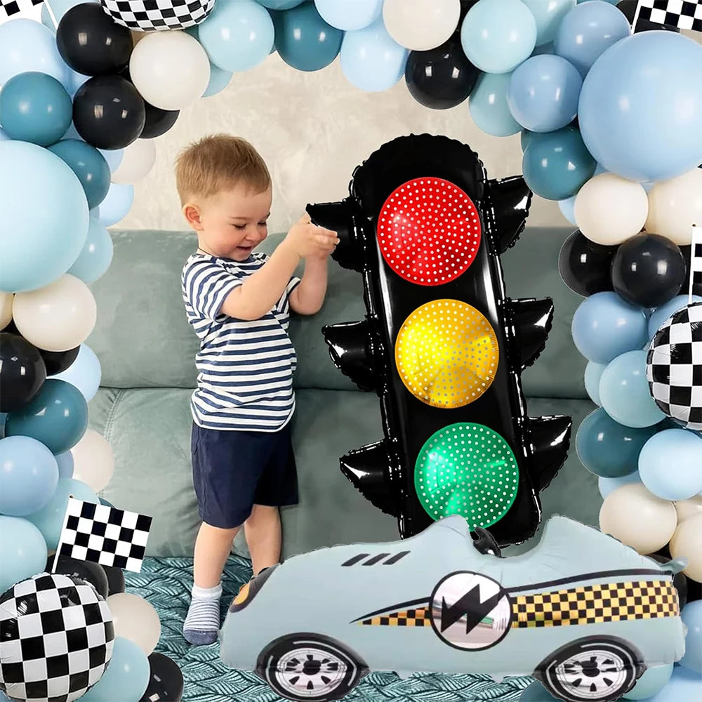A race car shaped balloon is positioned in front of a black traffic light balloon set and a young child.