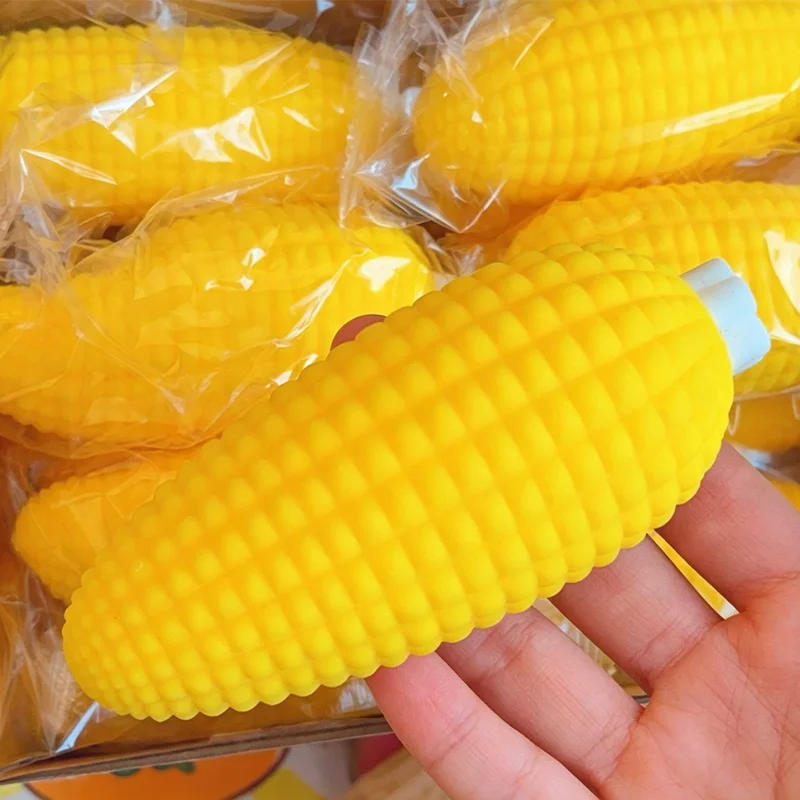 A hand holds a bright yellow squishy food-shaped stress ball corn in clear packaging.