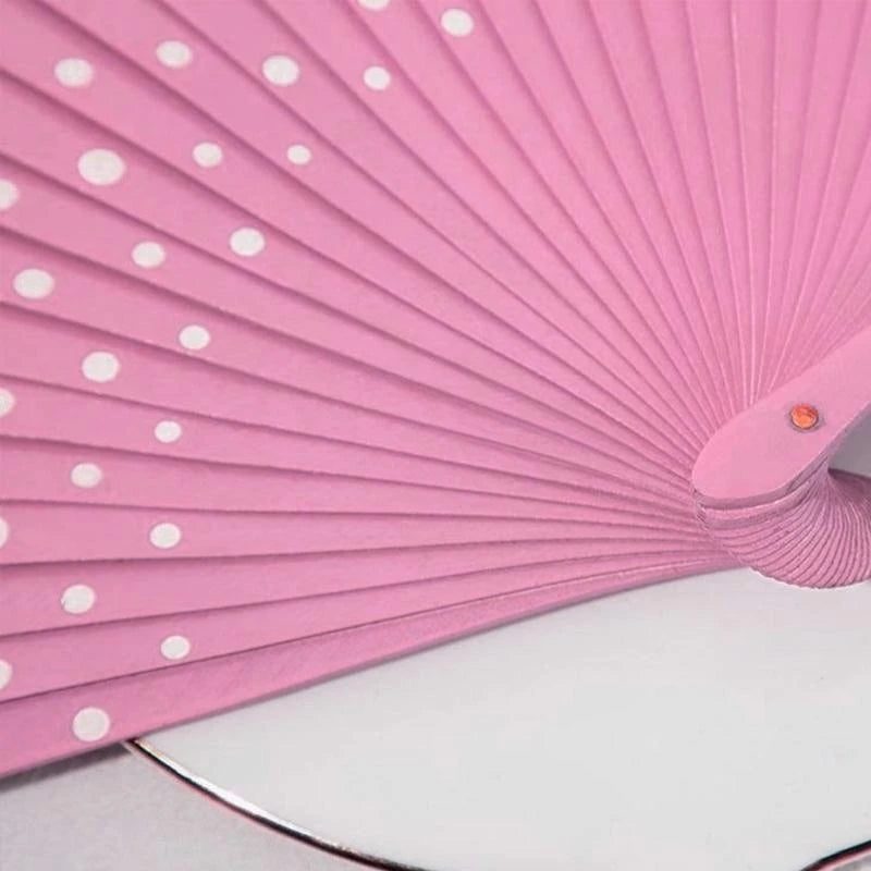 A pink wooden hand fan with pleated ribs and white polka dots shown in a close-up angle.
