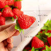 A hand holds a bright red artificial strawberry, showing its size and texture against a white background.