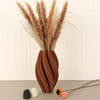 A tall arrangement of dried grasses in a textured terracotta vase on a light surface.