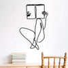Black line art drawing of a person sitting and holding a book on a white wall above a wooden table.