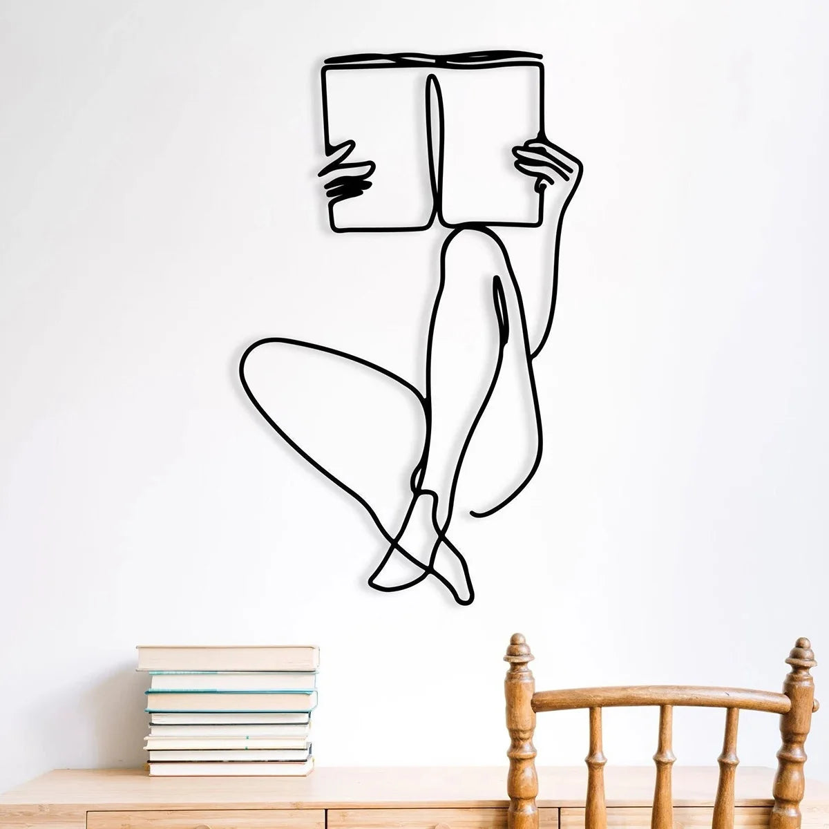 Black line art drawing of a person sitting and holding a book on a white wall above a wooden table.
