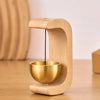 A wooden door bell with a brass bowl and hanging wind chime is displayed on a wooden surface.