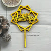 A gold acrylic birthday cake topper featuring the words Happy Birthday shaped like a hexagon on a stick.