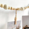 A beige beaded photo display garland with natural twine and wooden clips hanging on a white wall.