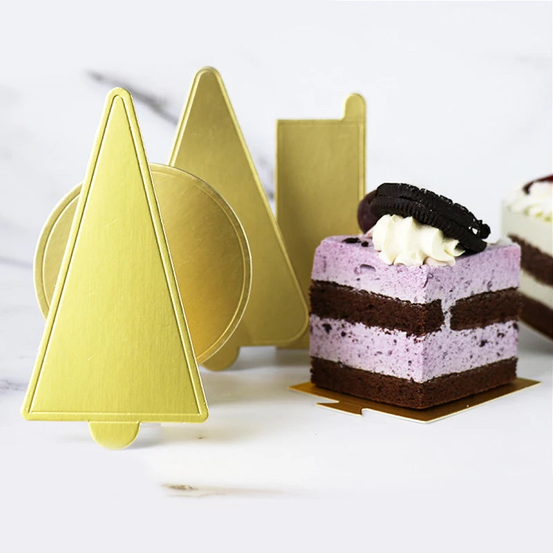 A stack of metallic gold dessert cake boards next to a slice of purple layer cake topped with white cream and a dark chocolat