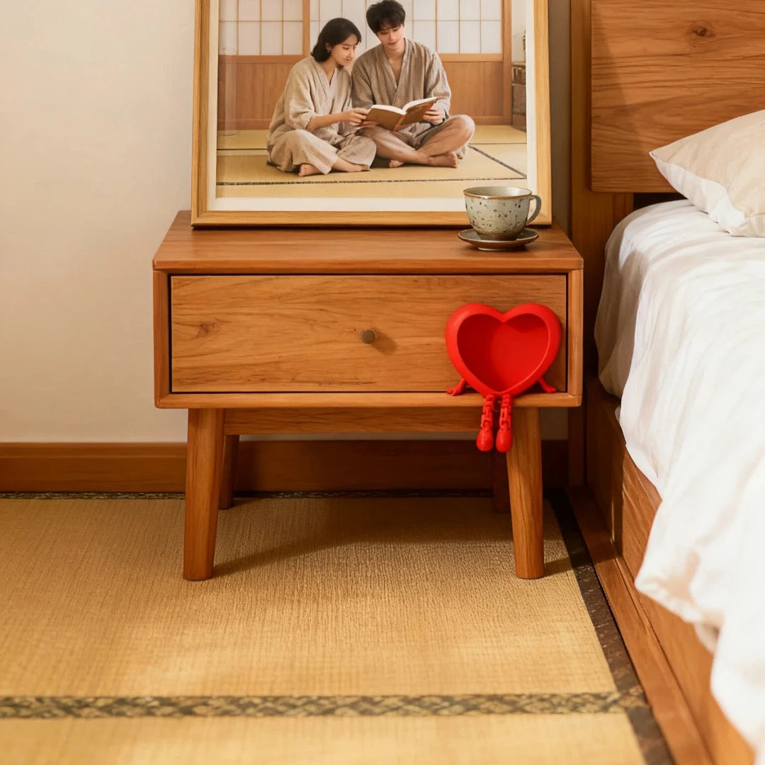 A wooden nightstand with a framed photo of two people and a red heart ornament on the front.