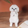 Petite statue de chien en résine blanche et duveteuse, pattes jointes, sur une surface en bois.