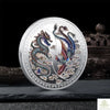 A commemorative coin featuring a Chinese dragon and phoenix design on a silver background.