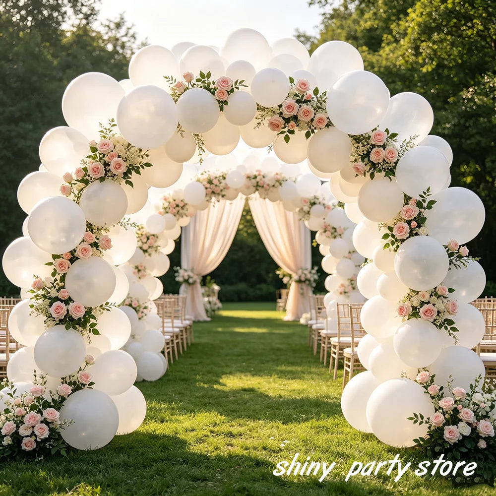 A floral archway made of matte white latex balloons decorated with pink roses and greenery for an event backdrop.