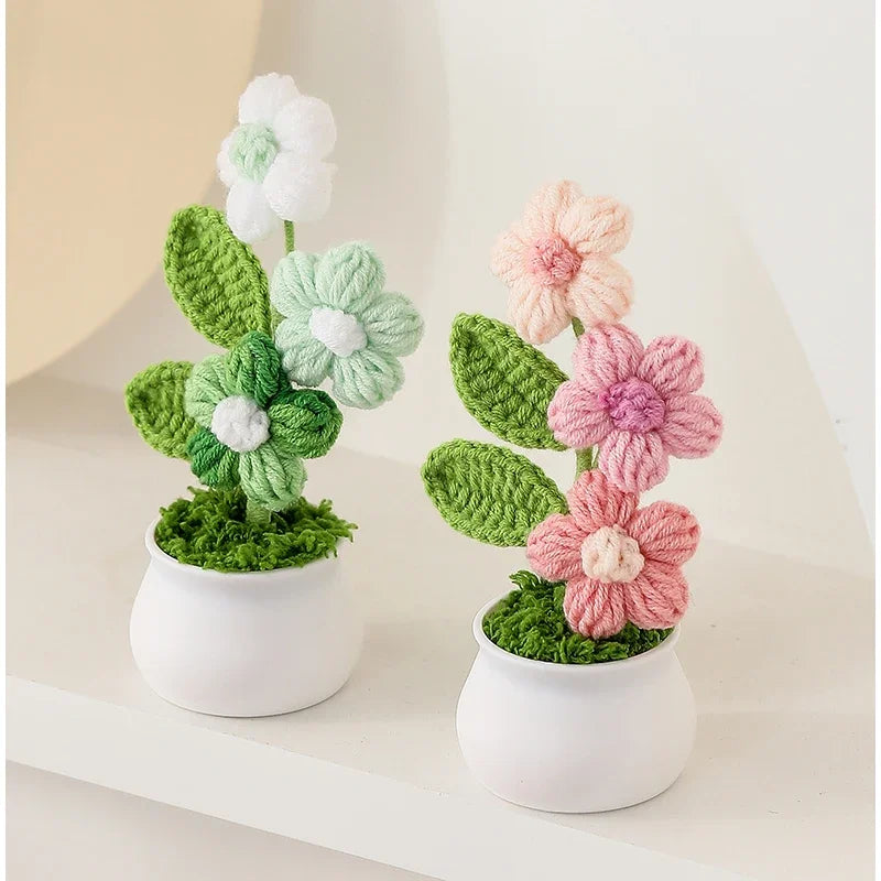 Hand woven crochet flowers in shades of white, green, and pink potted in white ceramic containers.