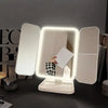 An LED trifold makeup mirror with adjustable lighting is displayed on a dark surface.